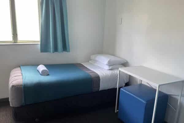 Single bed with desk and armchair in a modern hostel room