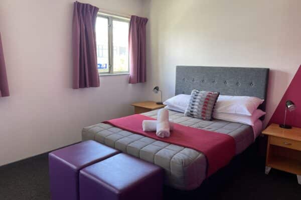 Double room featuring a double bed with reading lights, plush towels, and stylish ottomans at Accents YHA Hostel Nelson